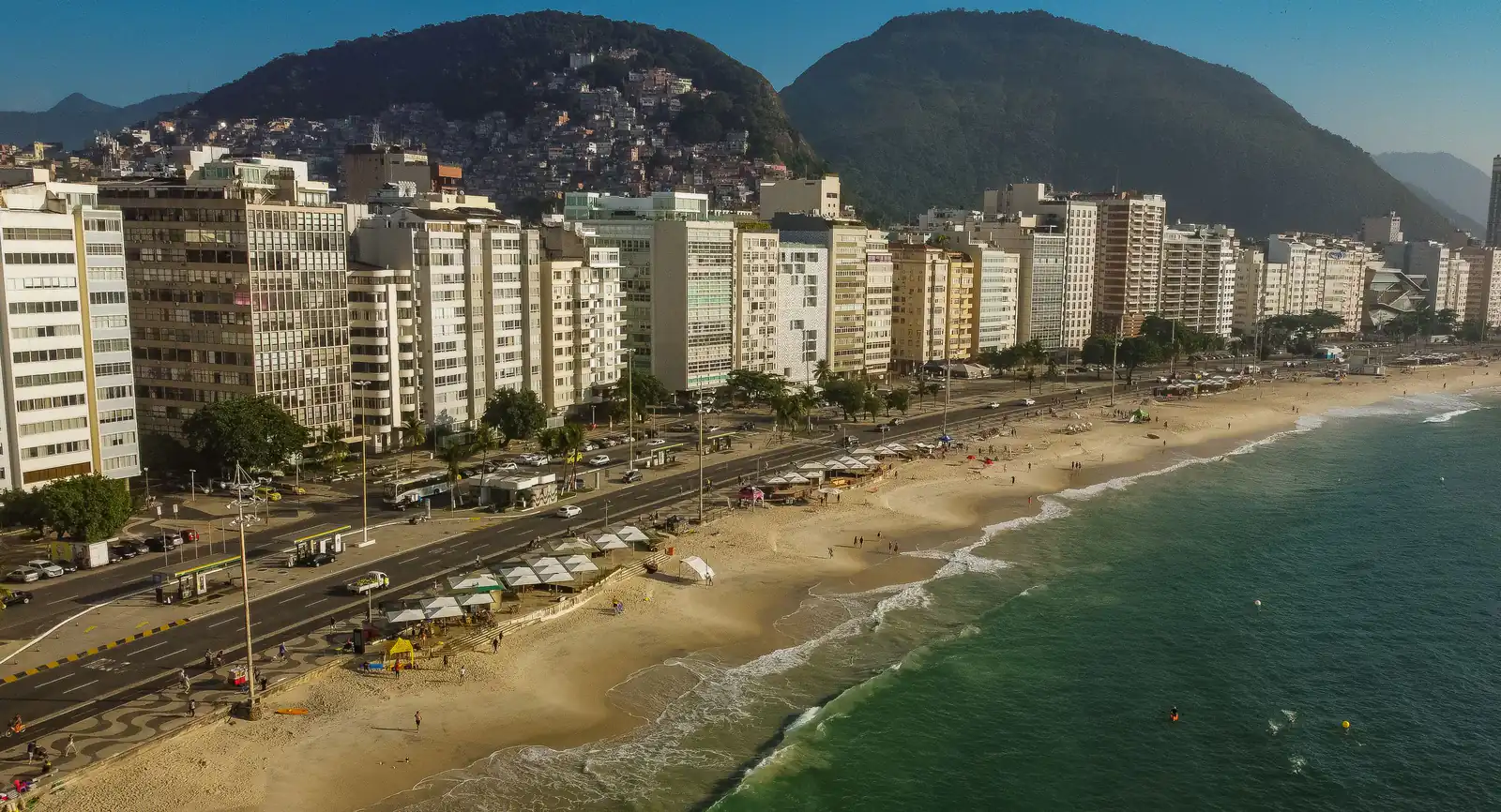 Vista elevada da Avenida Atlântica, em Copacabana, com a fileira de prédios residenciais de frente para a praia e os morros ao fundo
