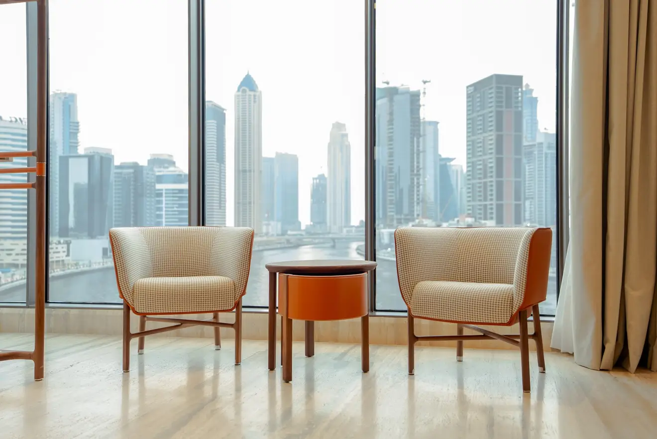 Duas poltronas de design diante de uma janela do chão ao teto, com vista para os prédios de uma cidade ao fundo