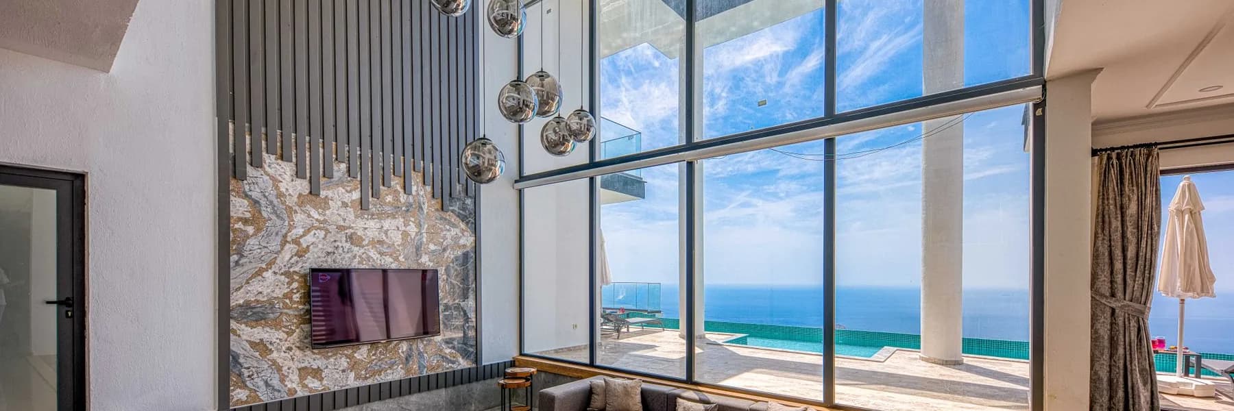 Sala de estar de pé-direito duplo com paredes de vidro do piso ao teto e vista para o mar, em imóvel de alto padrão, representando o patrimônio que o dono mantém e continua usando durante uma operação de home equity