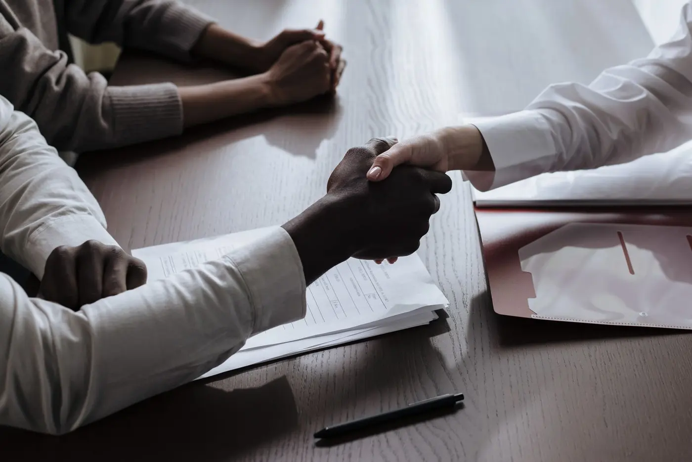 Aperto de mãos sobre uma mesa com contrato e documentos, selando uma operação de crédito