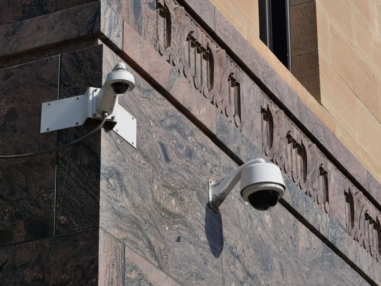 Duas câmeras de segurança tipo domo instaladas na quina de granito da fachada de um prédio