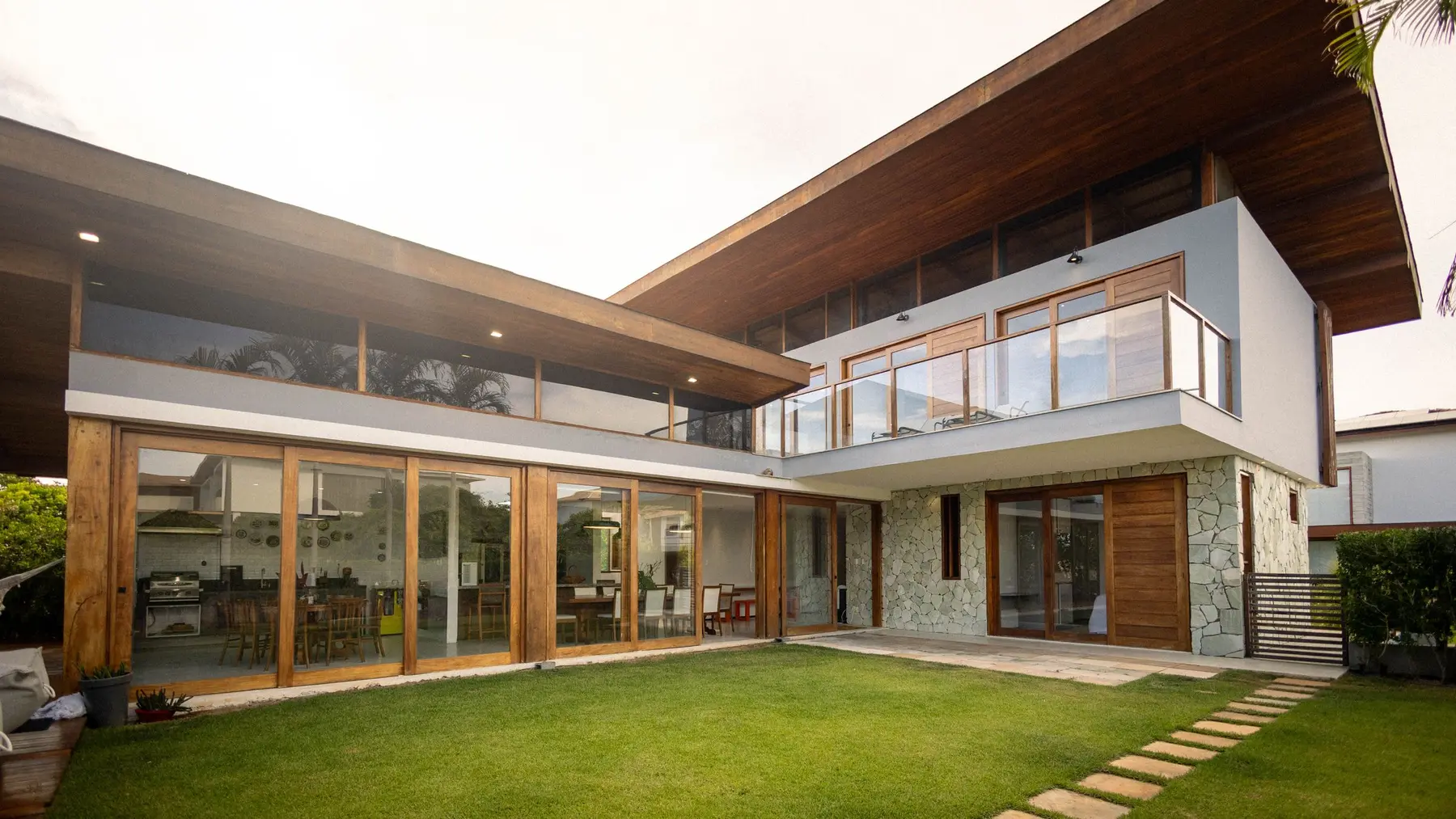 Casa contemporânea de alto padrão com fachada de madeira, pedra e amplas portas de vidro voltadas para o jardim, representando o imóvel de alto valor usado como garantia no home equity Usecasa do Santander