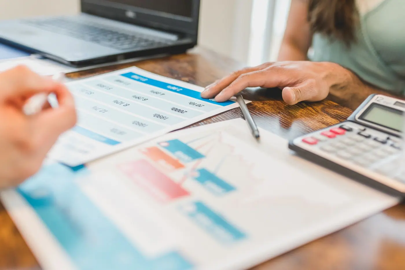 Duas pessoas comparando relatórios financeiros com gráficos e tabelas, calculadora e notebook sobre a mesa, analisando propostas de crédito antes de assinar