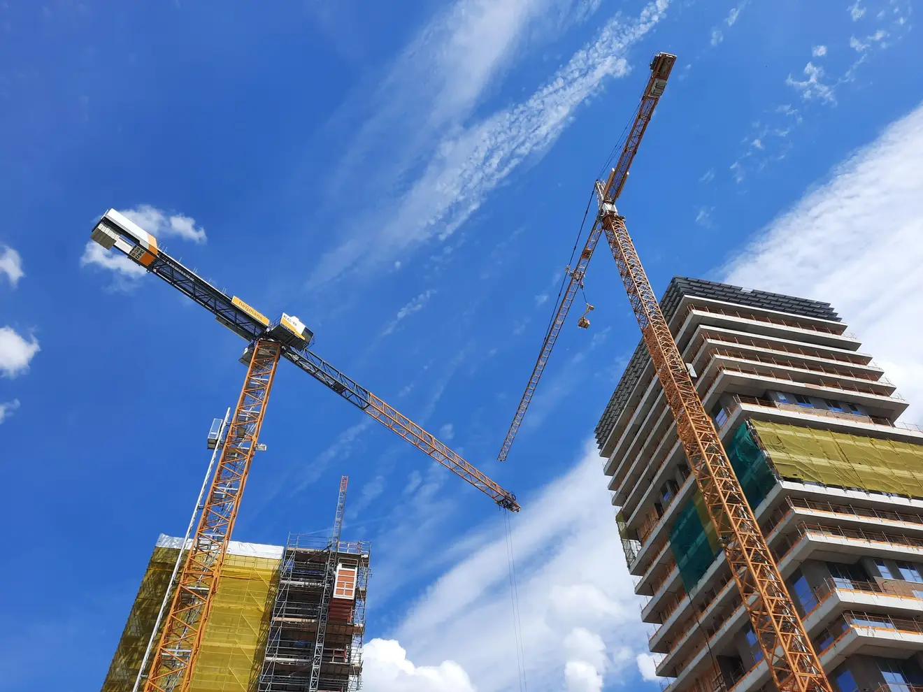 Duas gruas de construção erguem torres residenciais de apartamentos contra um céu azul