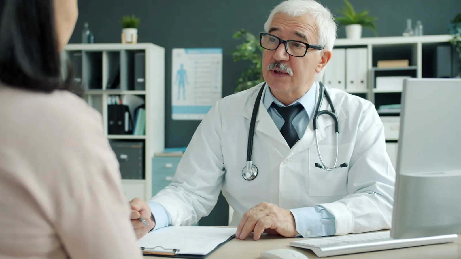 Médico experiente em jaleco branco conversando com paciente em consultório real — perfil profissional típico que recorre ao home equity para expansão de clínica ou aquisição de equipamento