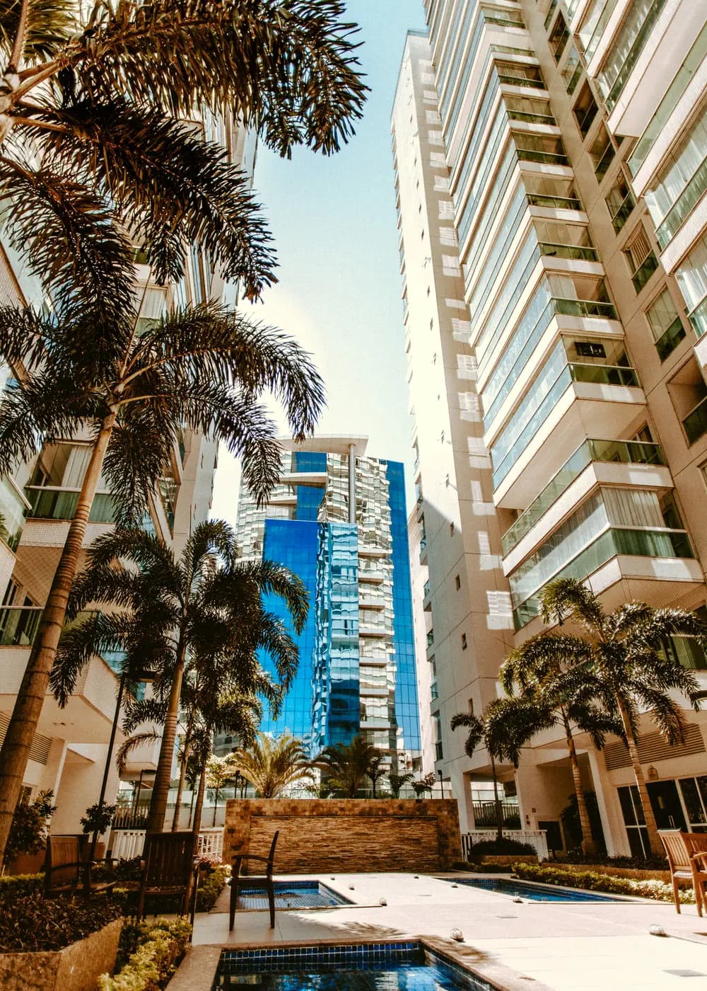 Piscina de condomínio entre torres residenciais e palmeiras