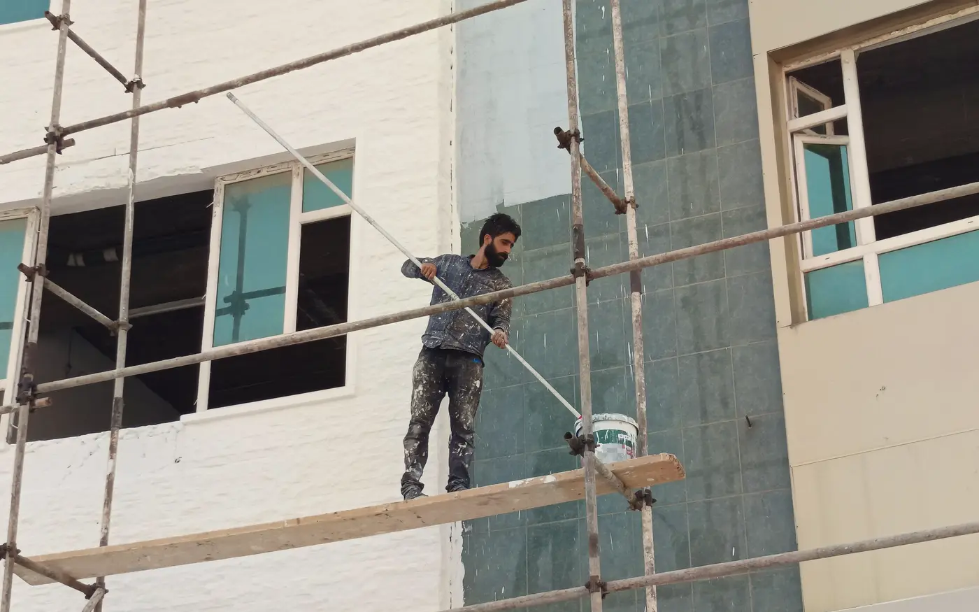 Pintor em andaime pintando a fachada de um prédio residencial