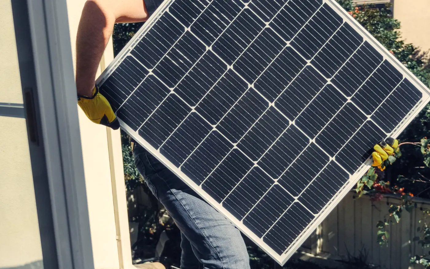 Técnico carregando um painel solar sobre um telhado de telhas cerâmicas